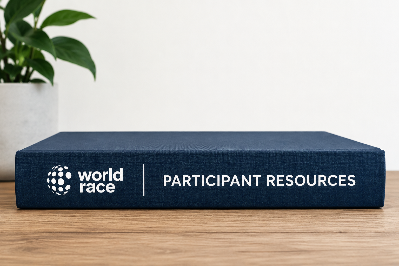 Navy hardcover book labeled World Race Participant Resources on a wooden desk
