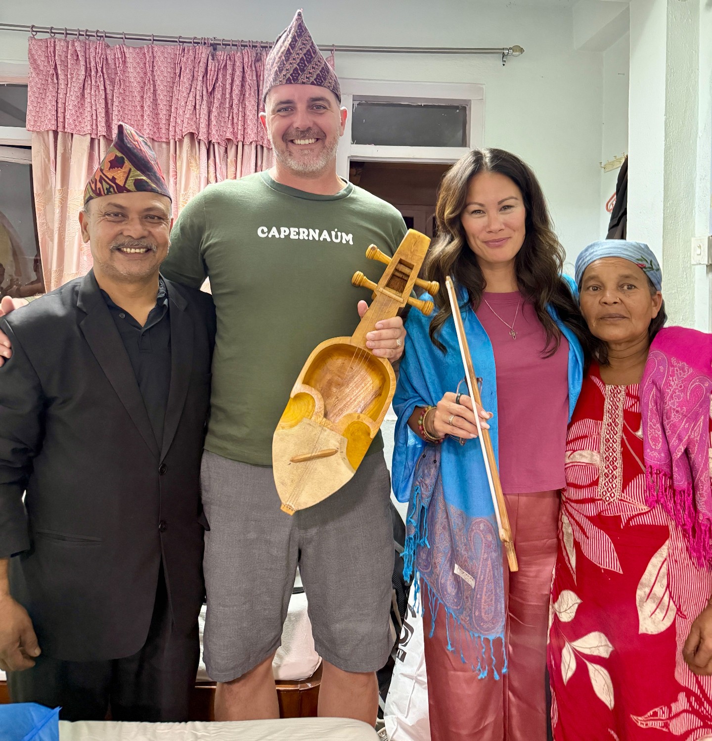A Parent Vision Trip family standing with local Nepali ministry hosts, holding a traditional handmade instrument