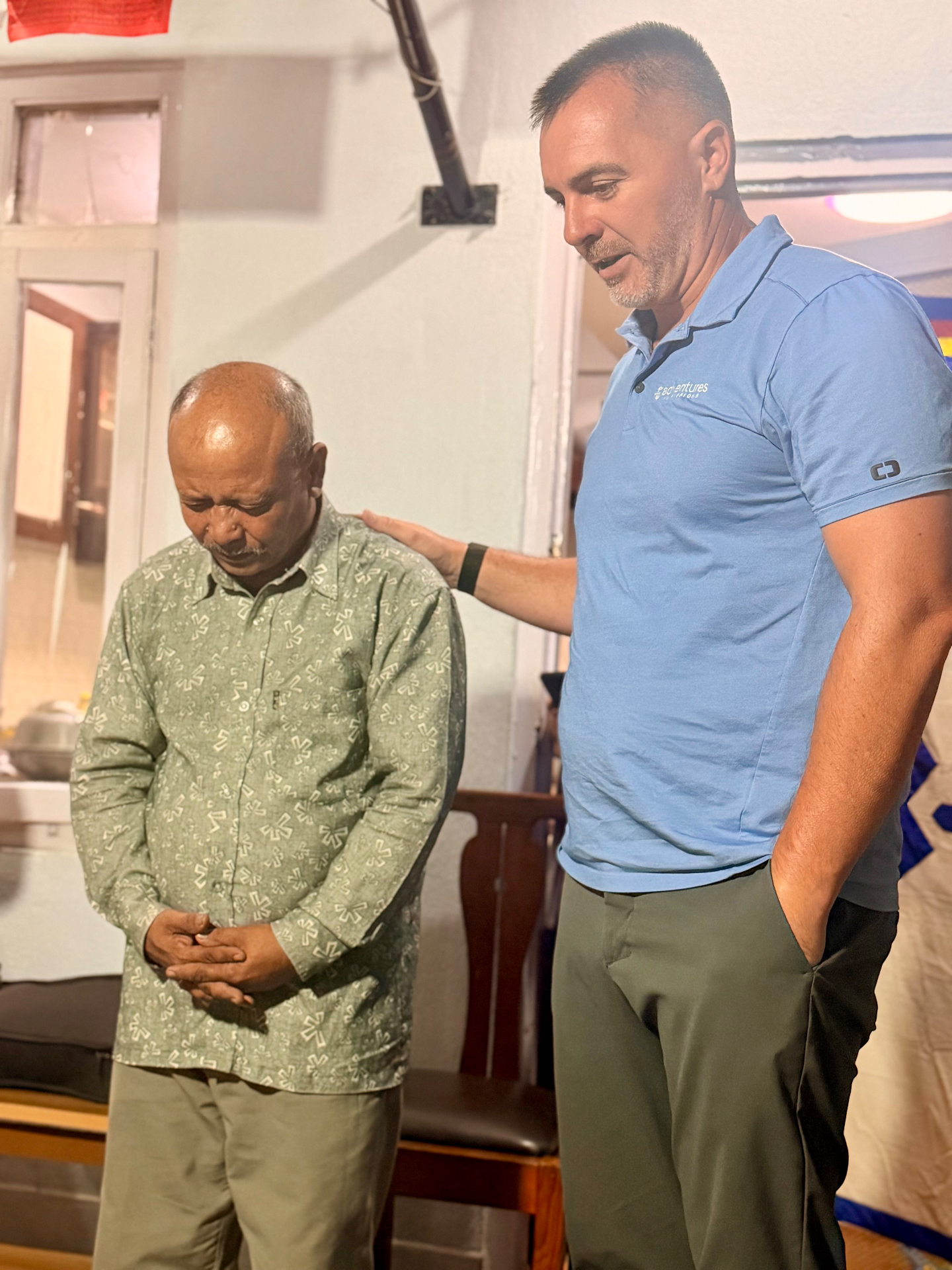 An Adventures in Missions leader praying over a local Nepali pastor with a hand on his shoulder