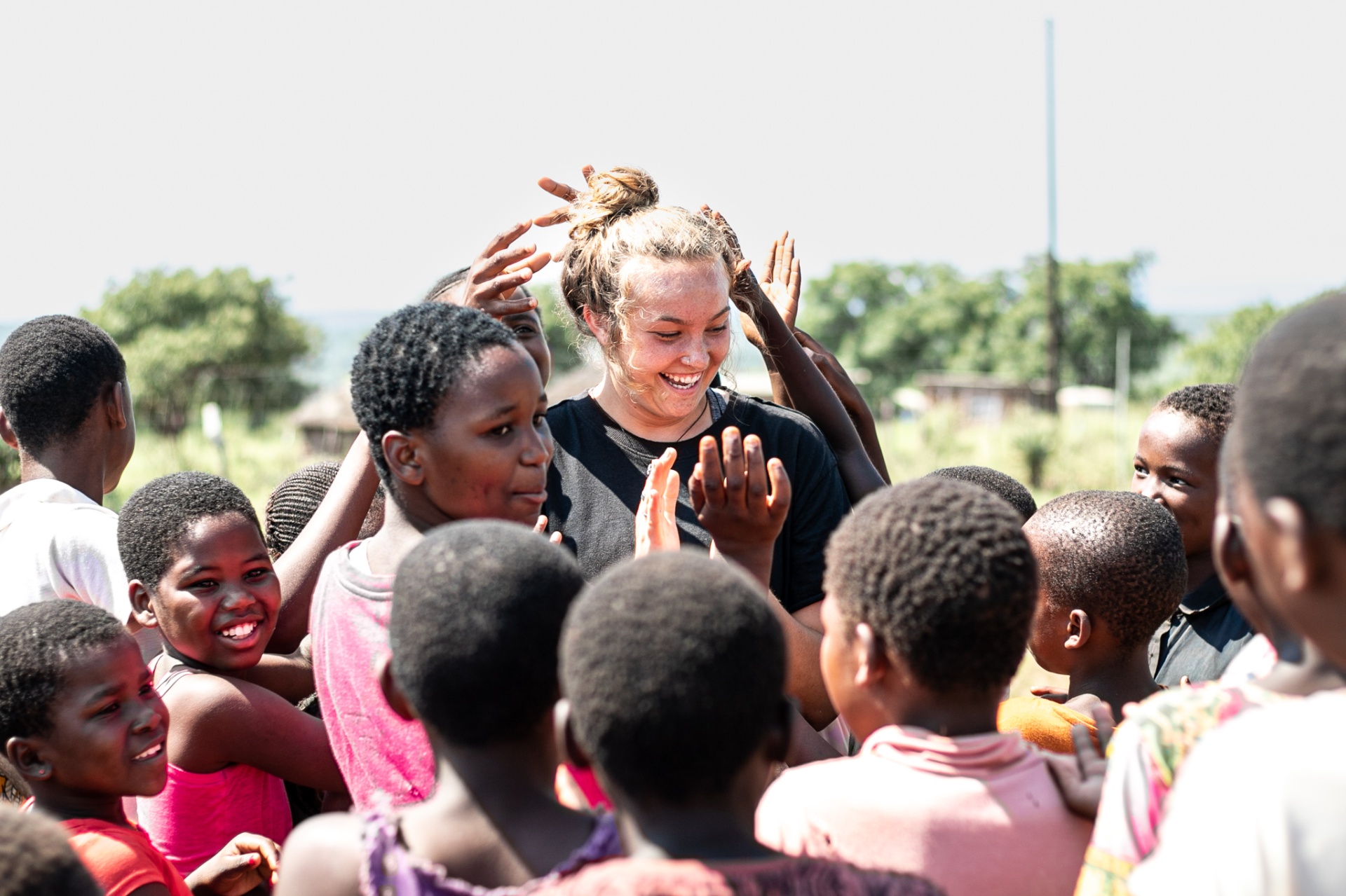 A World Race participant laughing with a group of kids who are reaching out to high-five and touch her hair